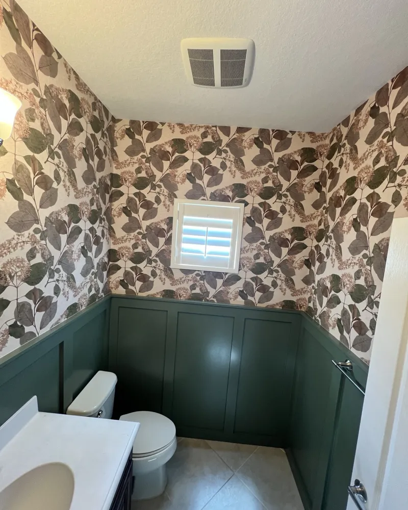 After: the same half bath with green board-and-batten wainscoting and botanical wallpaper above