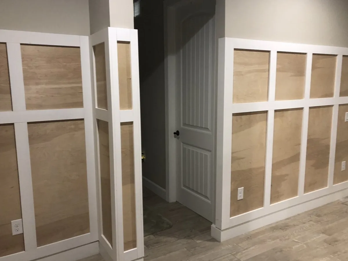 During: board-and-batten wainscoting built with plywood panels and white trim grid, wrapping a corner and doorway