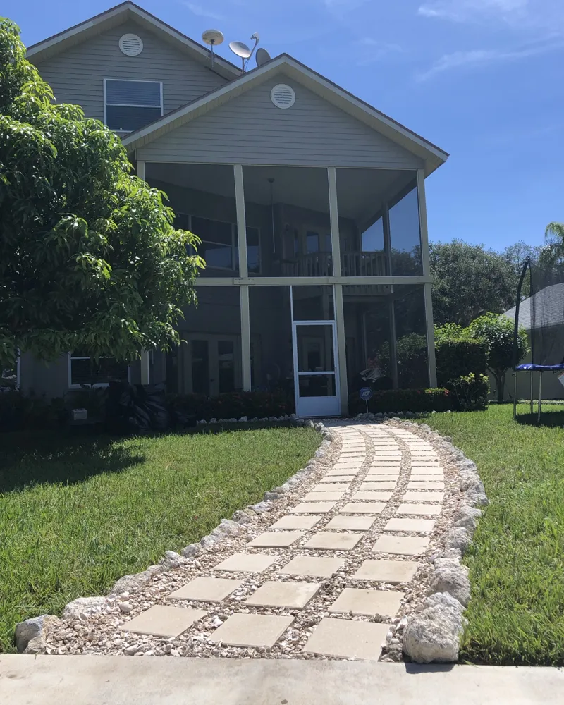 After: curved walkway of square pavers set in shell rock with natural stone borders leading to the lanai