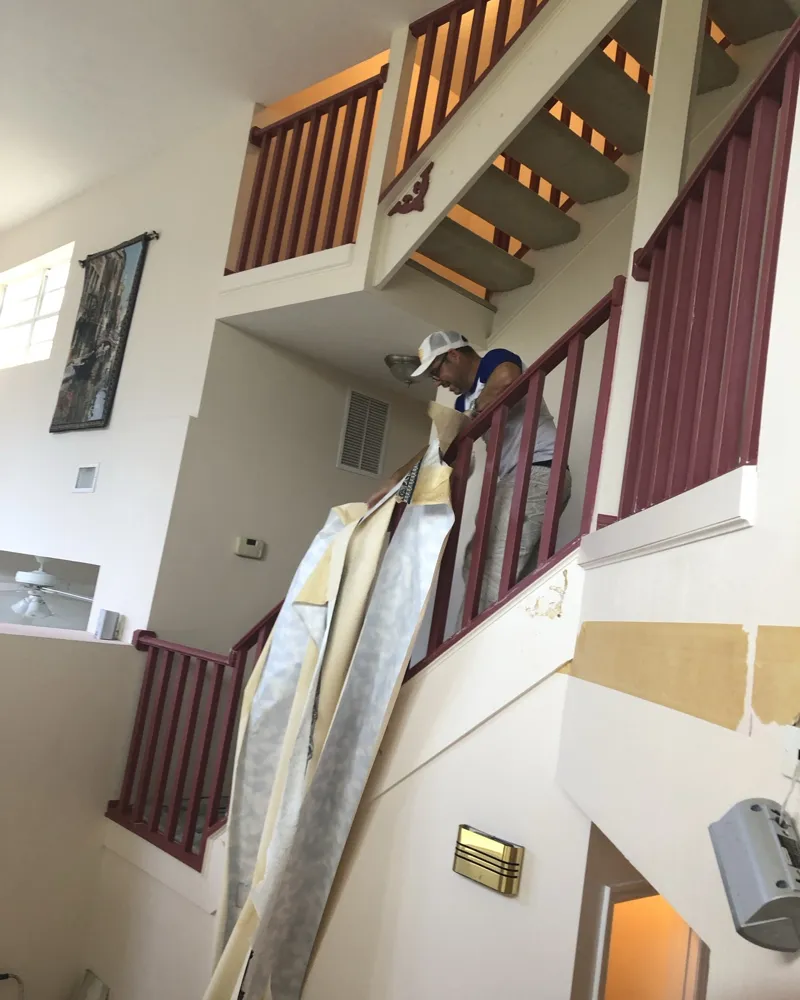Before: two-story stairwell with maroon railings while old wallpaper is stripped from the walls