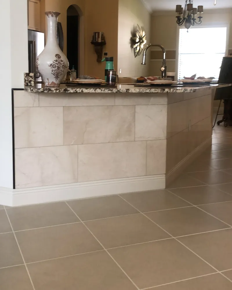After: the kitchen bar wall clad in large cream marble-look tile with a finished edge trim and baseboard