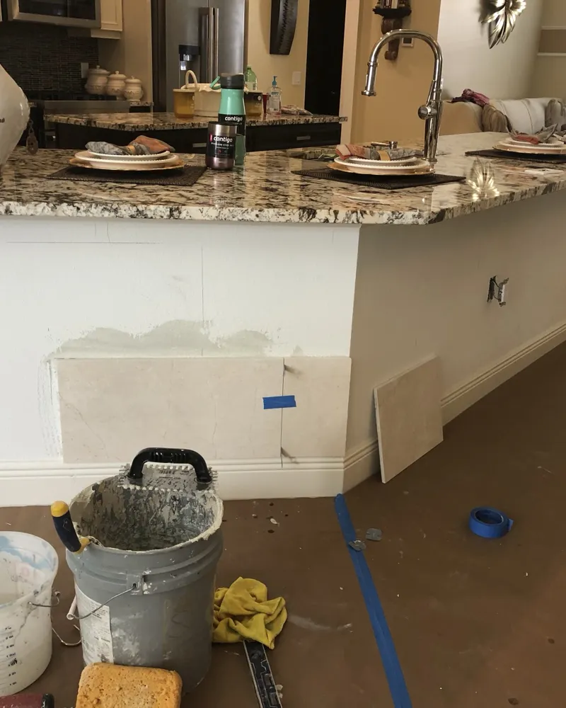 Before: kitchen bar wall below a granite counter, layout lines drawn and first large stone-look tiles dry-fit, floor protected