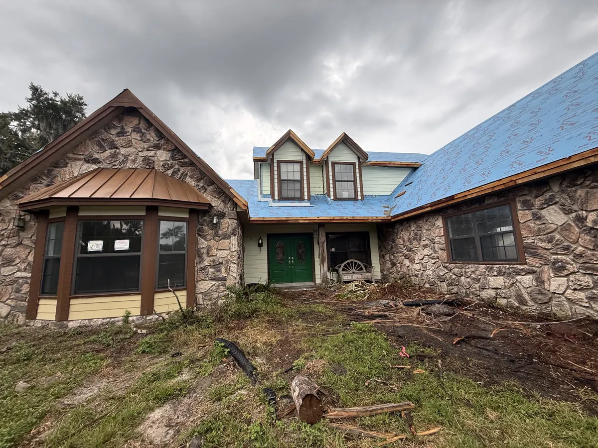 Before: two-story stone and siding home in Country Wood Estates, Sarasota, with brown trim and an overgrown yard