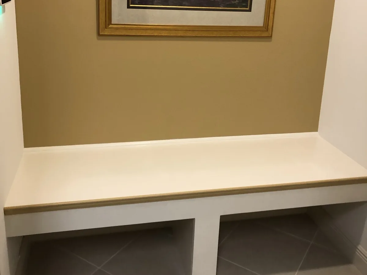 After: finished built-in bench with a smooth white top, gold-trimmed edge and two open cubbies below