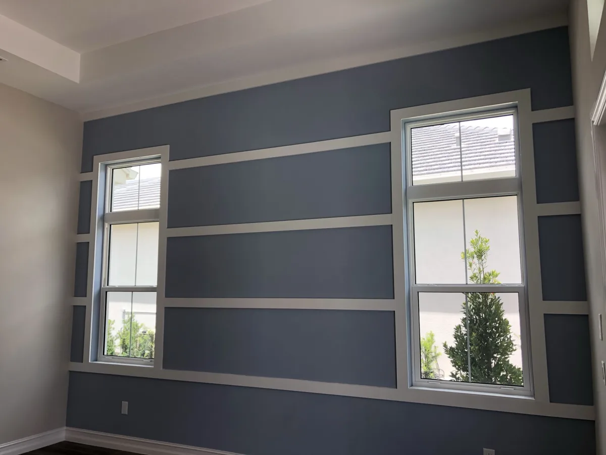 After: custom grid of white trim boards framing both windows across a slate-blue accent wall