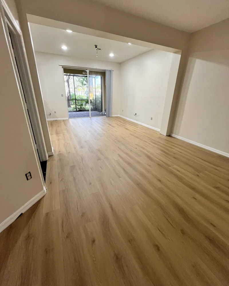 After: the half wall removed into one open room, new light oak luxury vinyl plank, warm neutral paint and new recessed lights