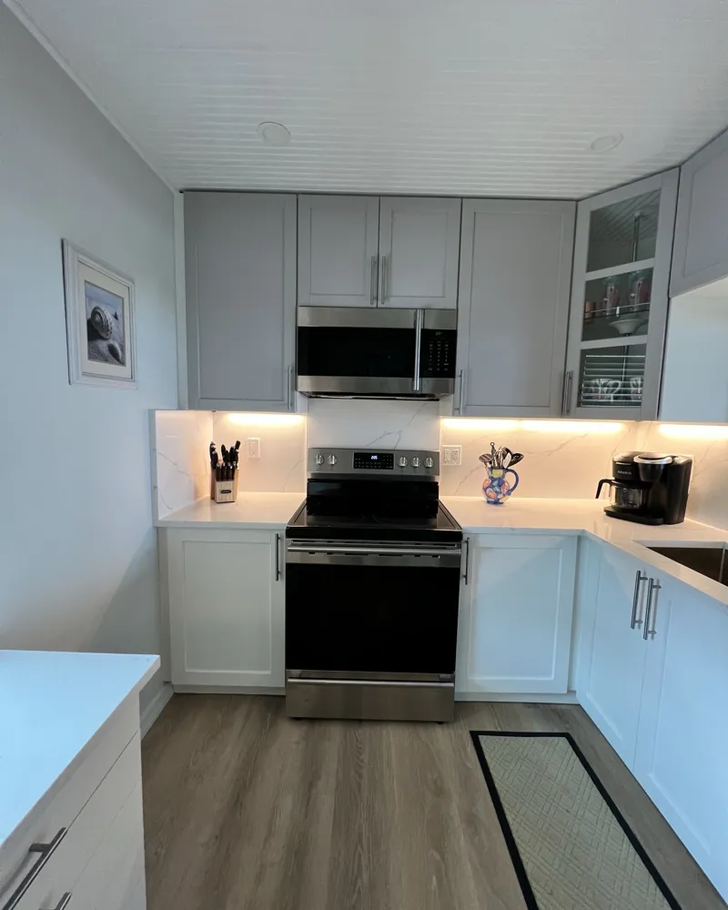 After: finished kitchen with two-tone shaker cabinets, white quartz counters and full-height backsplash, under-cabinet lighting, beadboard ceiling and wood-look floor