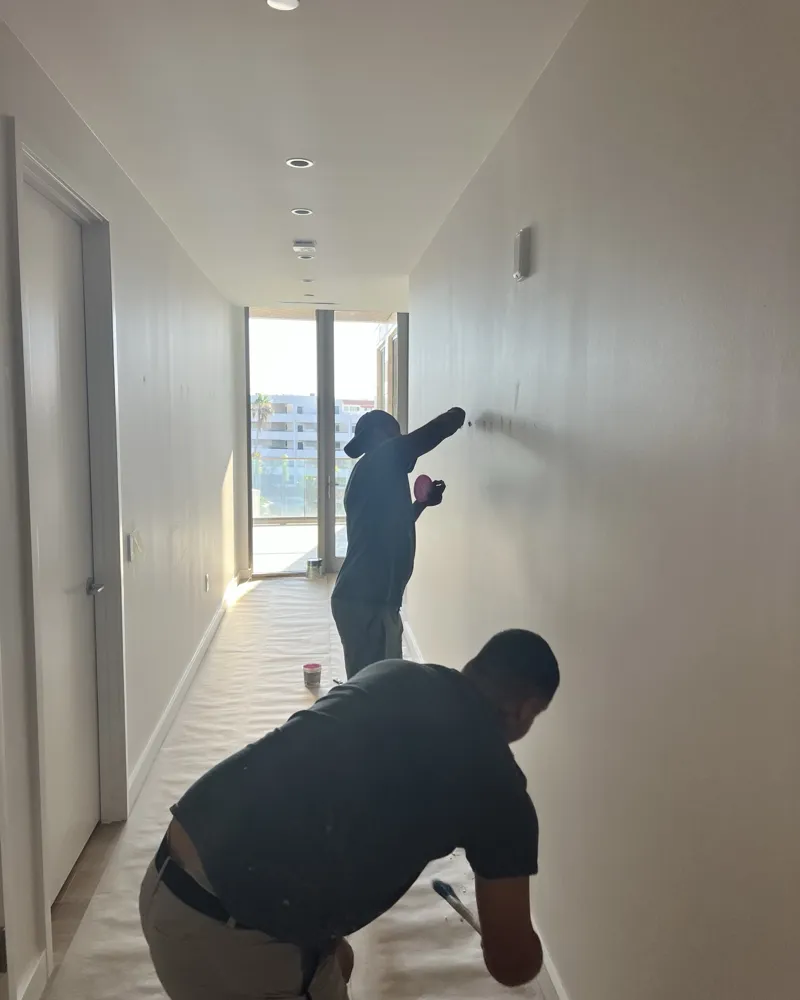 Prep: crew patching and sanding hallway walls with floors covered in protective paper