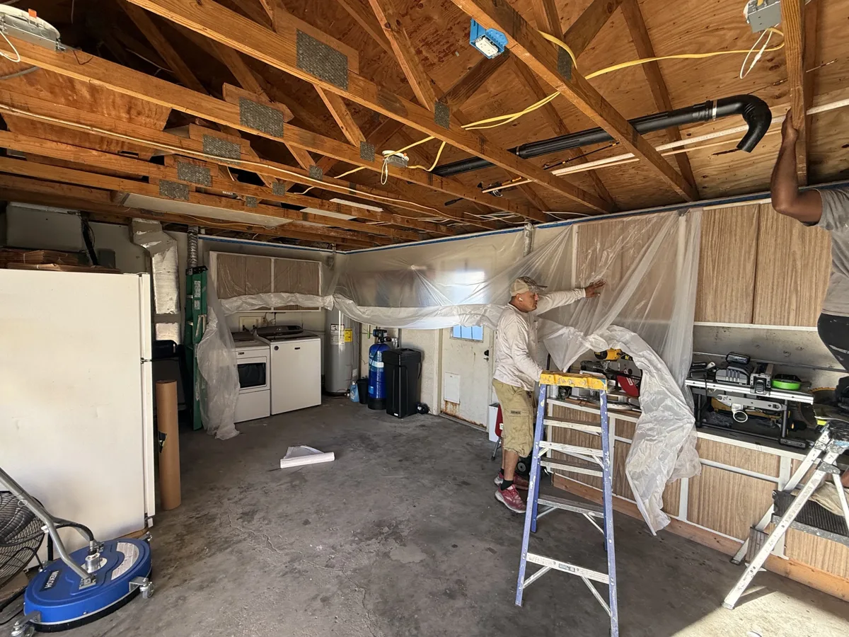 Before: garage ceiling open to the trusses while the crew hangs plastic to protect appliances and cabinets