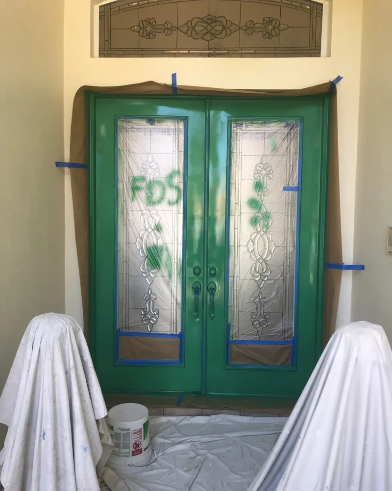 Process: double entry doors freshly sprayed green, with the decorative glass fully masked and the entry protected with paper and drop cloths