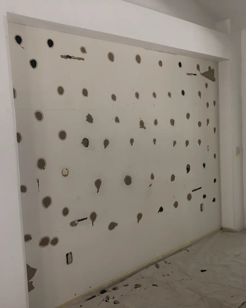 Before: recessed living room wall covered in dozens of anchor holes, torn drywall paper and old patches
