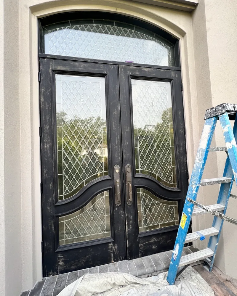 Before: arched double wood entry doors with sun-worn, peeling black finish and bare wood showing
