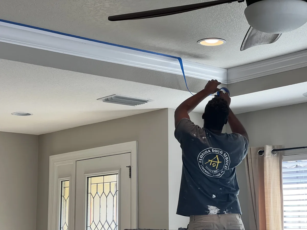 Process: crew member taping off the newly installed crown molding on a tray ceiling before painting