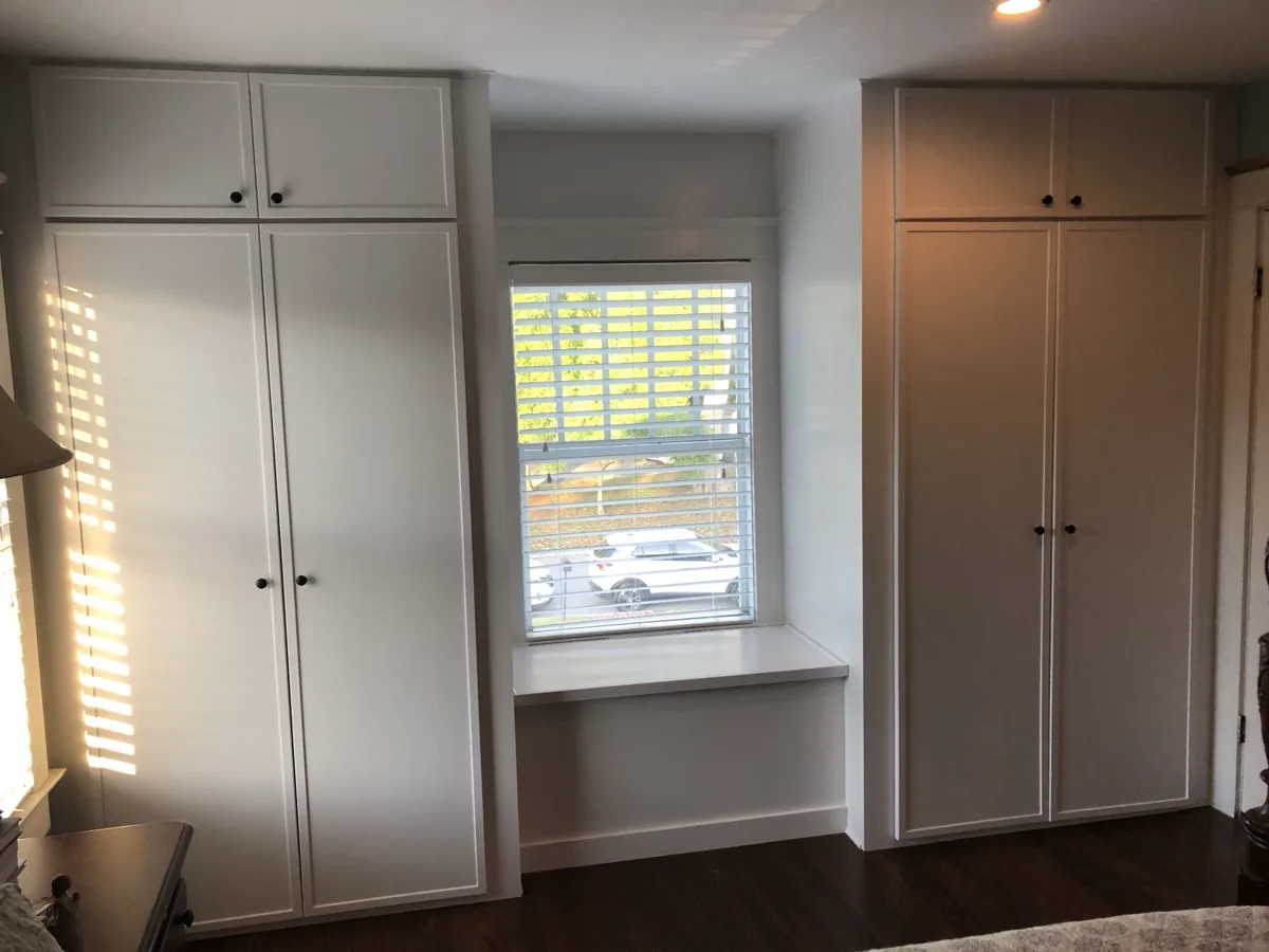 After: finished white custom closet wall with shaker doors, upper cabinets and a window seat between them
