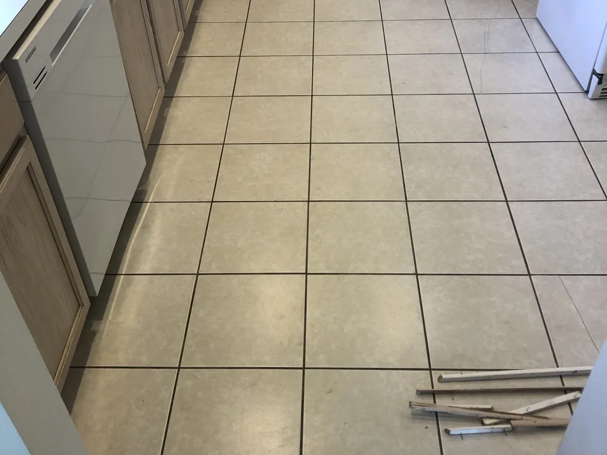 Before: kitchen with dated beige ceramic tile floor and dark grout lines